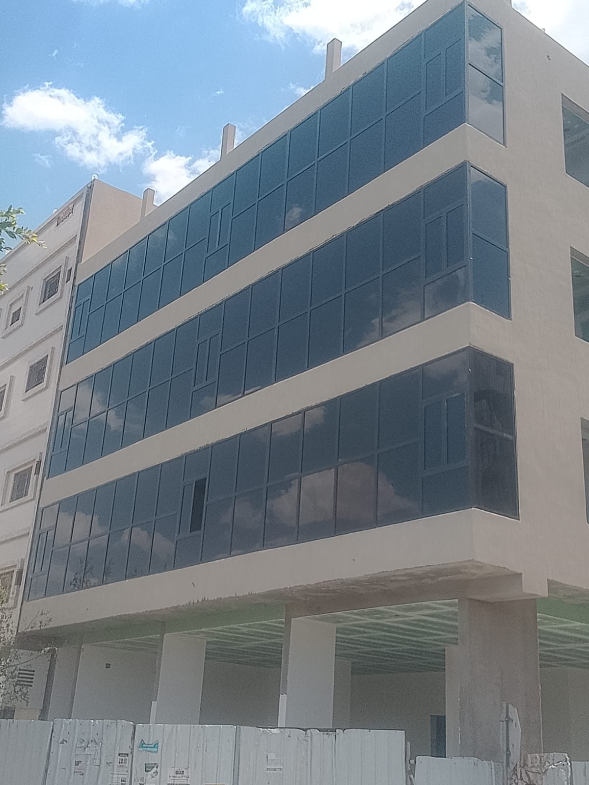واجهة زجاج سكريت أزرق عاكس بإطارات ألمنيوم تغطي ثلاثة أدوار من مبنى تجاري