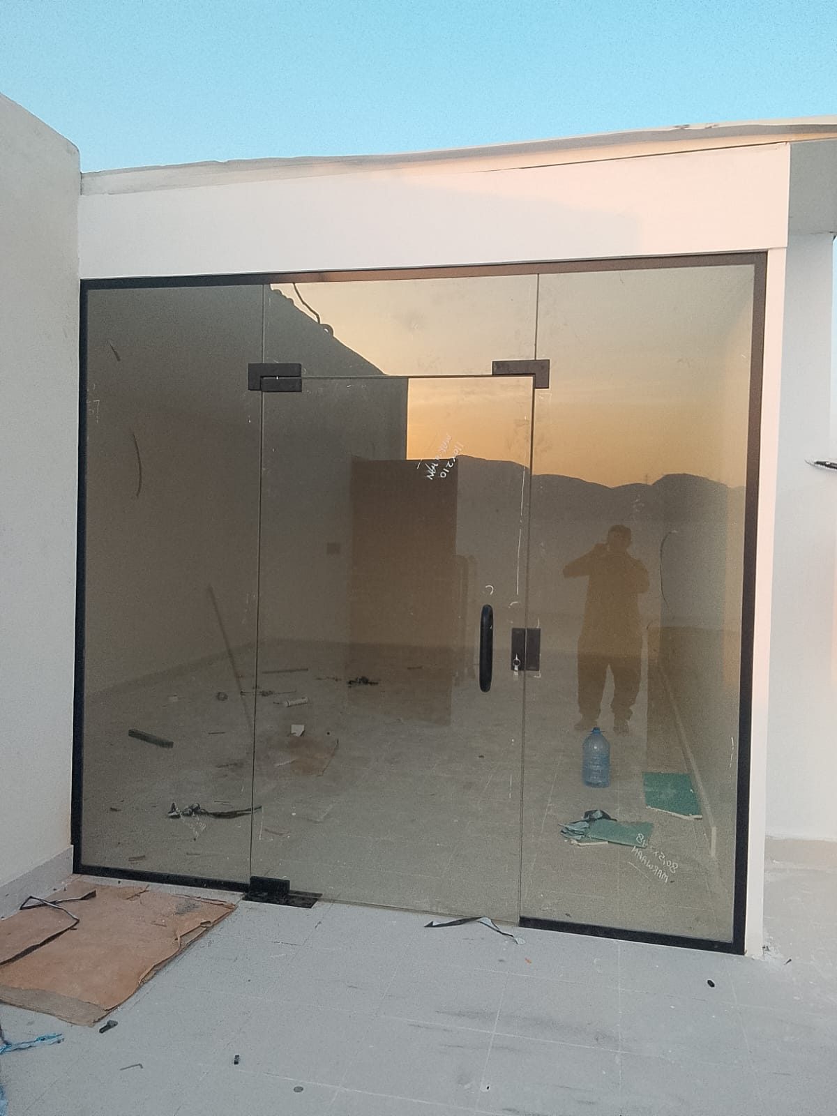 باب سكريت مزدوج بزجاج برونزي وإطار ألمنيوم أسود عند مدخل مبنى وقت الغروب